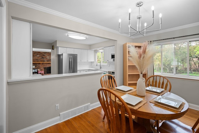 dining space with wood finished floors, a chandelier, baseboards, and crown molding