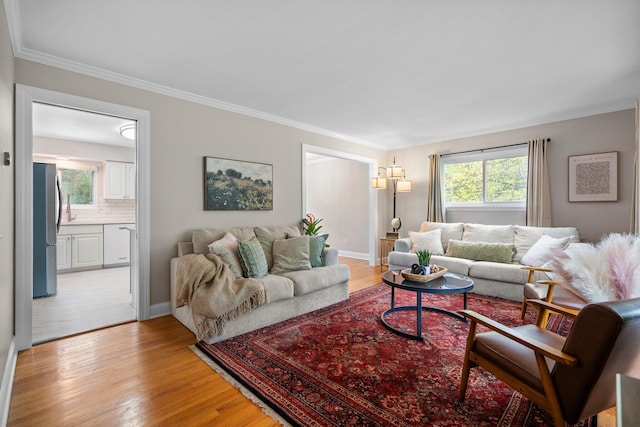 living area featuring light wood finished floors, plenty of natural light, ornamental molding, and baseboards