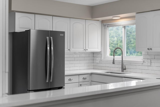 kitchen with freestanding refrigerator, a sink, white cabinets, decorative backsplash, and light countertops