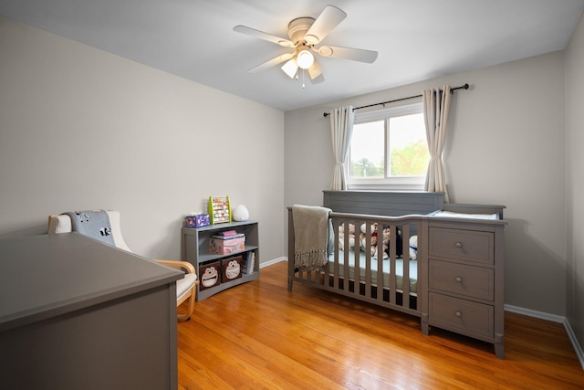 bedroom featuring light wood finished floors, baseboards, a nursery area, and a ceiling fan