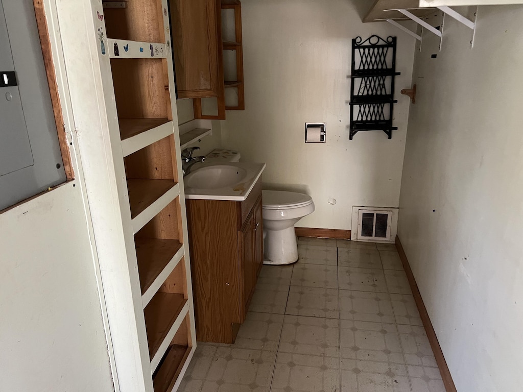 311 N Washington St, Charlotte, MI 48813 - half bathroom with baseboards, electric panel, toilet, vanity, and tile patterned floors