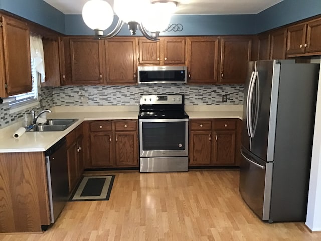 kitchen with appliances with stainless steel finishes, light wood-style floors, a sink, light countertops, and decorative backsplash