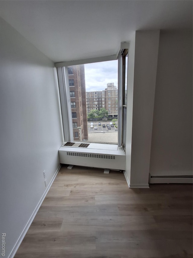 8200 E Jefferson Ave Unit 59/602, Detroit, MI 48214 - spare room featuring baseboard heating, wood finished floors, baseboards, and a view of city