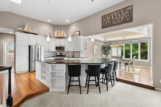 kitchen with appliances with stainless steel finishes, open shelves, dark countertops, a kitchen bar, and white cabinetry