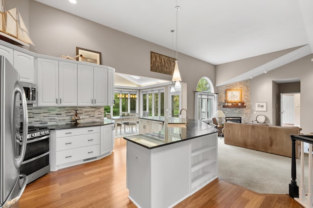 kitchen with appliances with stainless steel finishes, dark countertops, open floor plan, a stone fireplace, and backsplash