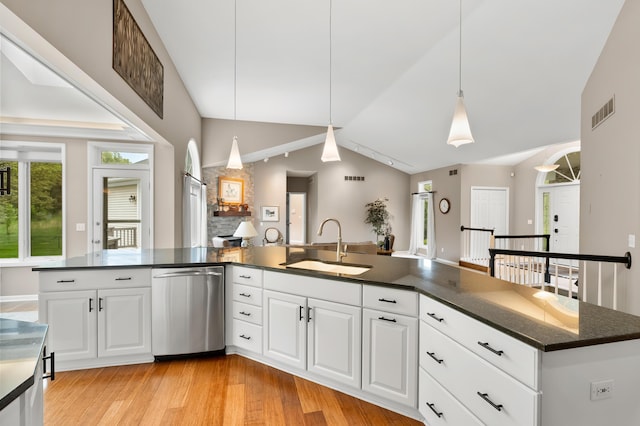 kitchen with stainless steel dishwasher, a sink, vaulted ceiling, light wood finished floors, and hanging light fixtures