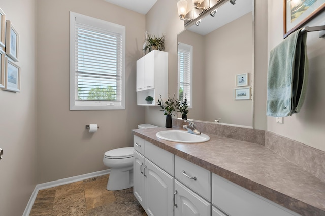 bathroom featuring baseboards, plenty of natural light, toilet, and vanity