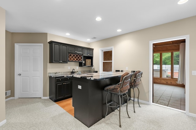 kitchen with a breakfast bar area, dark cabinets, baseboards, light colored carpet, and recessed lighting