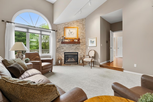 carpeted living room with high vaulted ceiling, track lighting, a stone fireplace, and baseboards