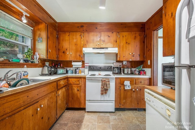 kitchen with white appliances, under cabinet range hood, a sink, and brown cabinetry