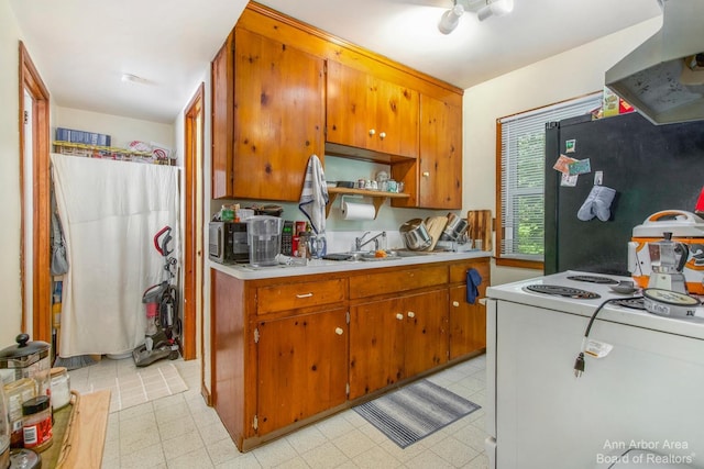 kitchen featuring exhaust hood, freestanding refrigerator, electric range, light countertops, and brown cabinetry