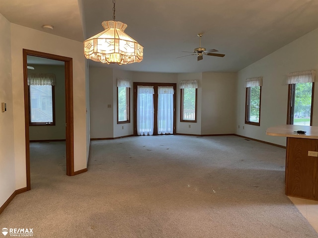 unfurnished living room with baseboards, light carpet, healthy amount of natural light, a chandelier, and vaulted ceiling