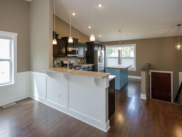 kitchen featuring stainless steel appliances, a peninsula, a breakfast bar area, dark wood-style floors, and a kitchen island