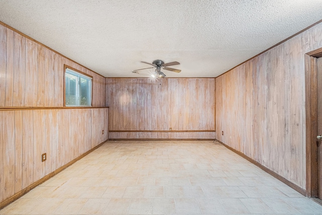 spare room with wooden walls, a ceiling fan, a textured ceiling, and baseboards