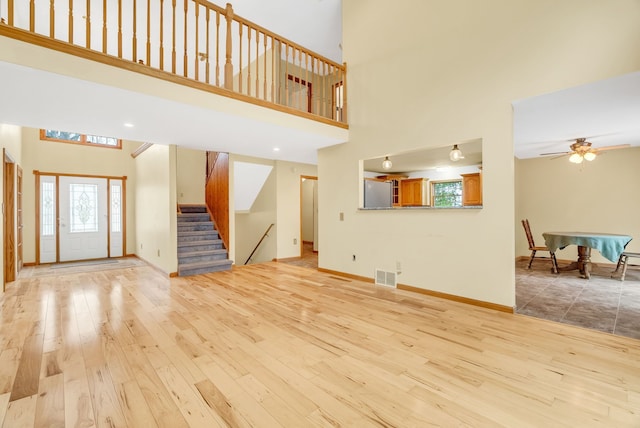 unfurnished living room with light wood finished floors, healthy amount of natural light, a high ceiling, stairway, and a ceiling fan