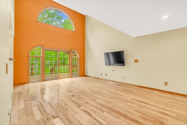 unfurnished living room with hardwood / wood-style floors, baseboards, a high ceiling, and recessed lighting