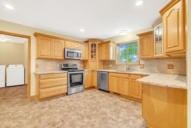 kitchen with stainless steel appliances, washing machine and dryer, a sink, tasteful backsplash, and glass insert cabinets