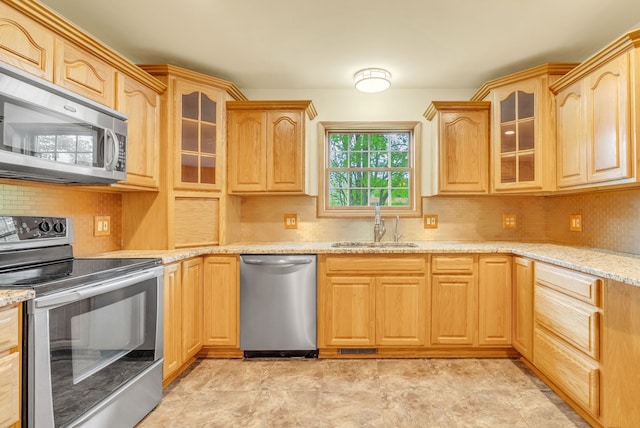 kitchen with stainless steel appliances, a sink, light brown cabinets, and backsplash