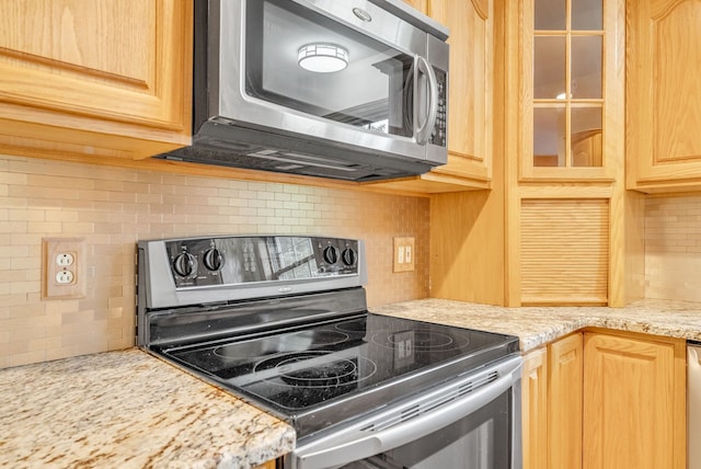 kitchen featuring appliances with stainless steel finishes, tasteful backsplash, glass insert cabinets, and light brown cabinetry