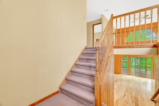 stairs with a towering ceiling, wood finished floors, and baseboards
