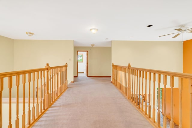 hall featuring carpet flooring, baseboards, and an upstairs landing