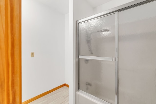 bathroom with wood finished floors, baseboards, and shower / bath combination with glass door