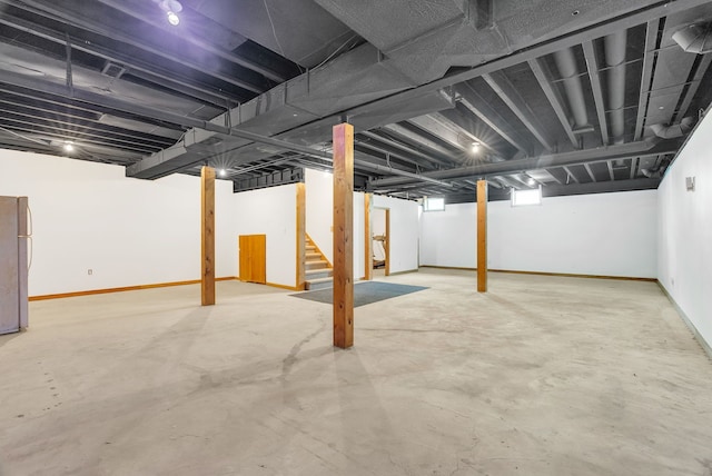 below grade area with stairway, freestanding refrigerator, and baseboards