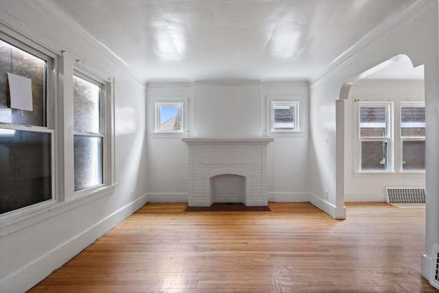 8916 Mendota St, Detroit, MI 48204 - unfurnished living room featuring a brick fireplace, light wood finished floors, arched walkways, crown molding, and baseboards