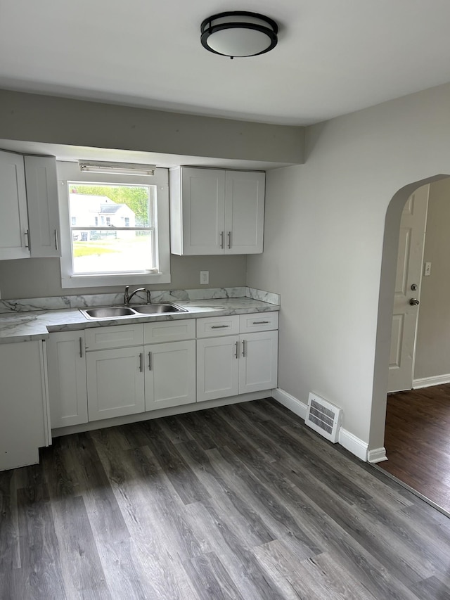 kitchen with a sink, light countertops, dark wood finished floors, arched walkways, and baseboards