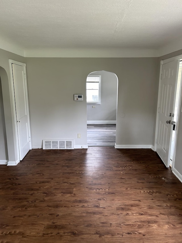 unfurnished room featuring arched walkways, dark wood-style floors, and baseboards