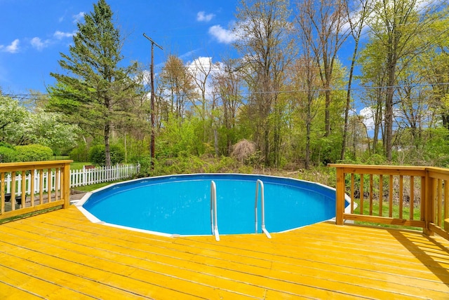 swimming pool with a wooden deck, fence, and view of scattered trees