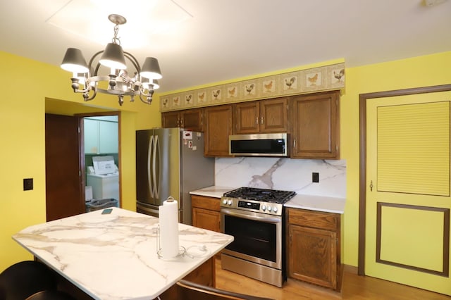 6452 Brian Circle Ln, Burton, MI 48509 - kitchen with stainless steel appliances, a chandelier, pendant lighting, decorative backsplash, and washing machine and clothes dryer