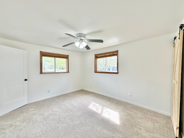 unfurnished bedroom with a barn door, carpet floors, baseboards, and a ceiling fan