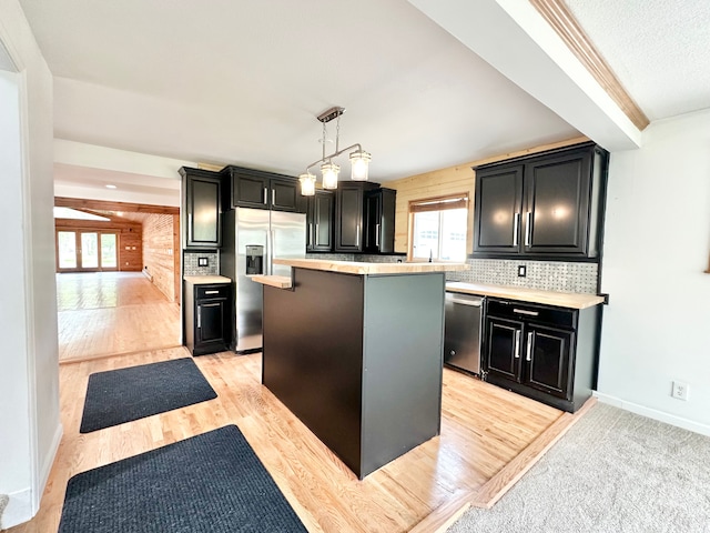 kitchen with dark cabinetry, stainless steel appliances, a kitchen island, and light countertops