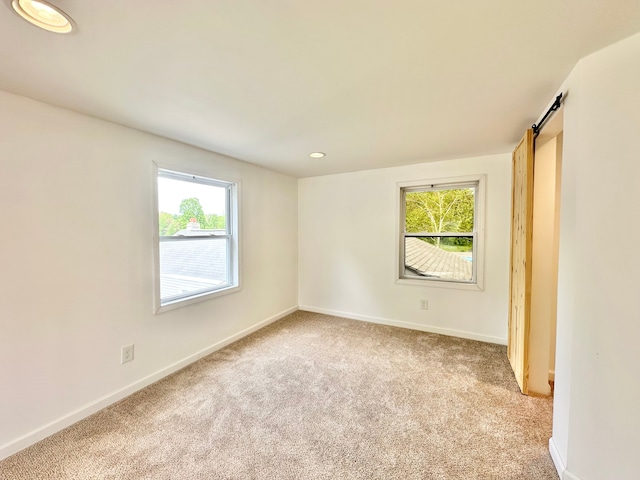 unfurnished room with light colored carpet, baseboards, recessed lighting, and a barn door