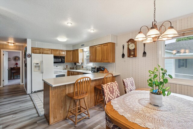 204 Crockett Dr, Quincy, MI 49082 - kitchen featuring white appliances, light wood-style floors, wallpapered walls, brown cabinets, and a peninsula