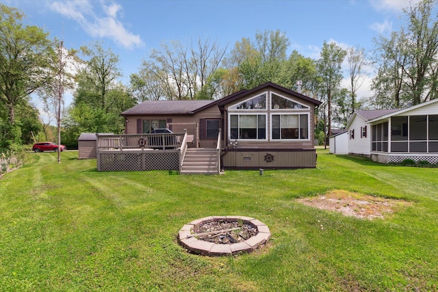 204 Crockett Dr, Quincy, MI 49082 - rear view of house featuring a fire pit, a sunroom, a deck, a storage unit, and a lawn