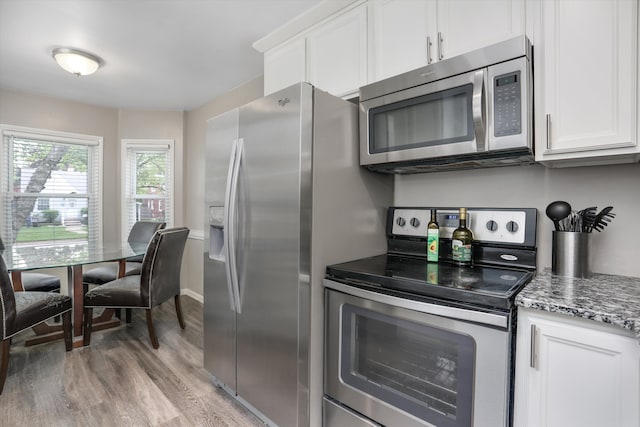 kitchen with stainless steel appliances, light wood-style floors, white cabinetry, and dark stone countertops