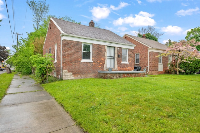 view of front of home with a chimney, brick siding, and a front yard
