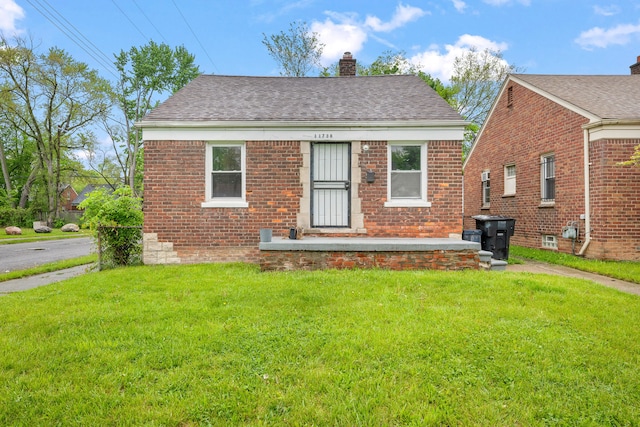 bungalow with a chimney, a front yard, and brick siding