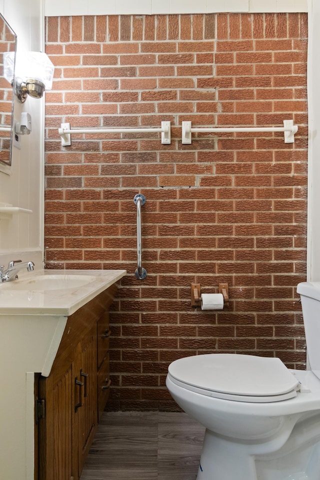 half bathroom featuring brick wall, toilet, and vanity