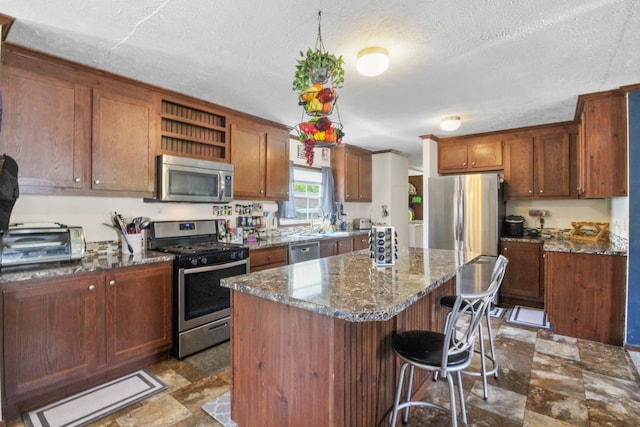 29878 Meadow Ln, Gibraltar, MI 48173 - kitchen featuring stainless steel appliances, a center island, a kitchen bar, dark stone countertops, and a textured ceiling