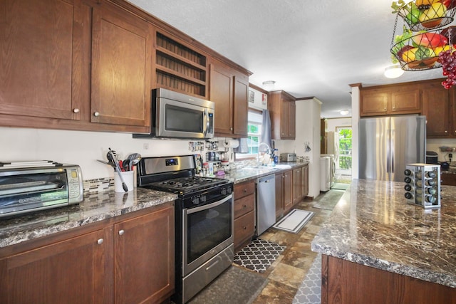 29878 Meadow Ln, Gibraltar, MI 48173 - kitchen with stainless steel appliances, independent washer and dryer, a sink, open shelves, and dark stone counters