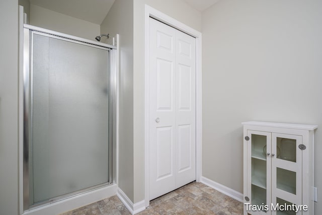 bathroom featuring a shower stall, stone finish floors, and baseboards