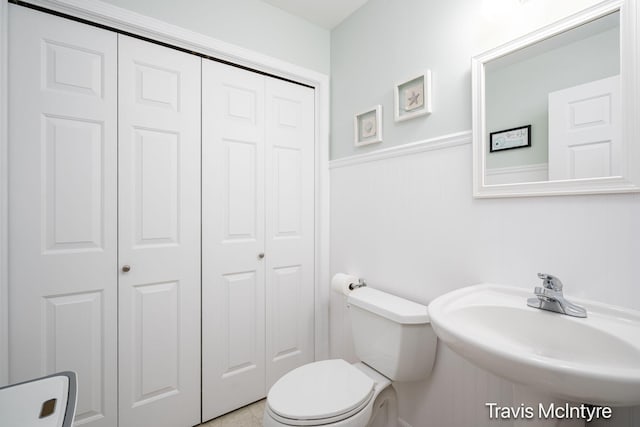 half bathroom with a closet, a sink, wainscoting, and toilet