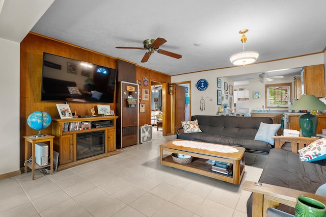 living room with a ceiling fan, wooden walls, light tile patterned floors, and ornamental molding