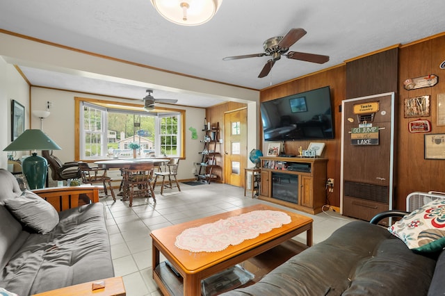living room featuring a ceiling fan, light tile patterned floors, wood walls, and ornamental molding