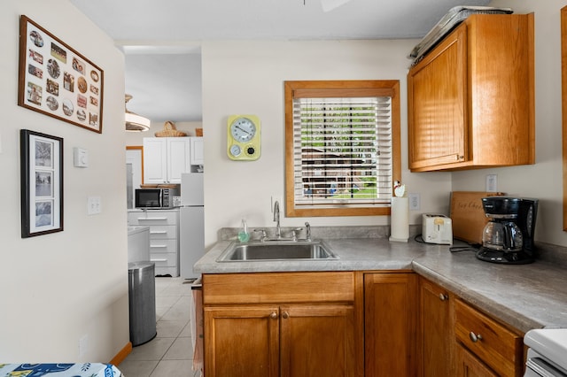 kitchen with a sink, freestanding refrigerator, light tile patterned floors, and brown cabinets