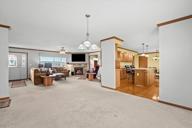 living room featuring light carpet, ornamental molding, a fireplace, baseboards, and a ceiling fan