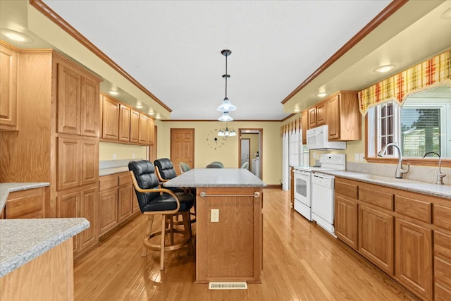 kitchen featuring white appliances, a sink, crown molding, a breakfast bar area, and light wood-type flooring